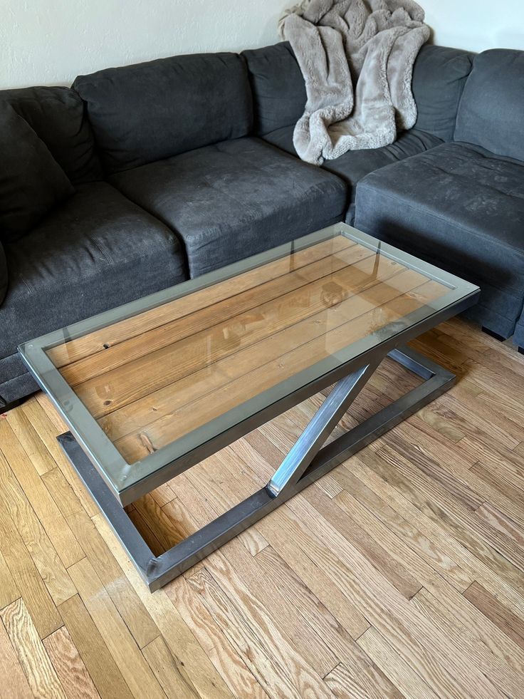 a glass coffee table sitting on top of a wooden floor next to a gray couch