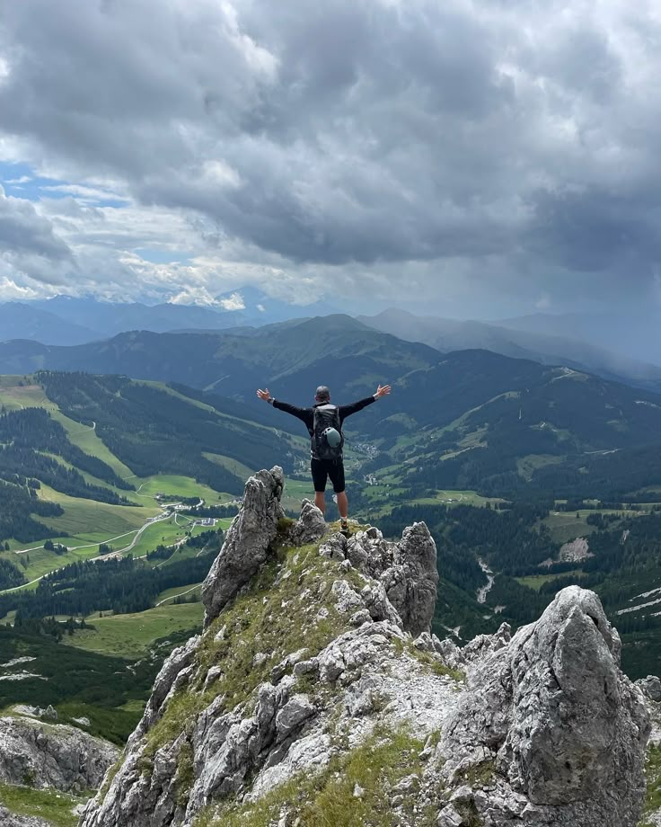 a man standing on top of a mountain with his arms wide open