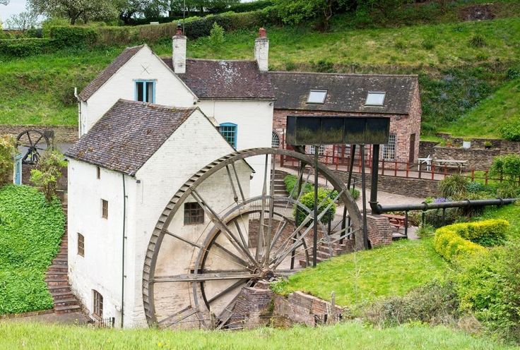 an old water wheel sits in front of a building on the side of a hill