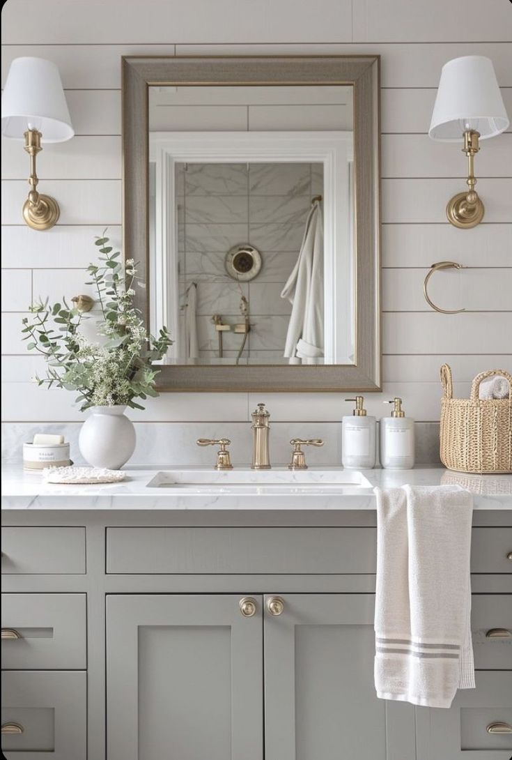 a bathroom with white walls and gold fixtures on the vanity, along with a large mirror