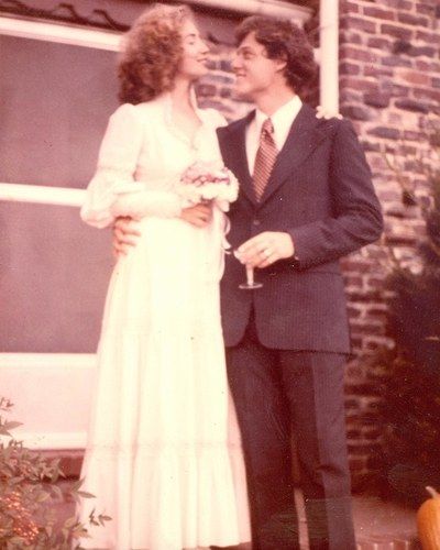 a man and woman standing next to each other in front of a brick building with pumpkins on the ground