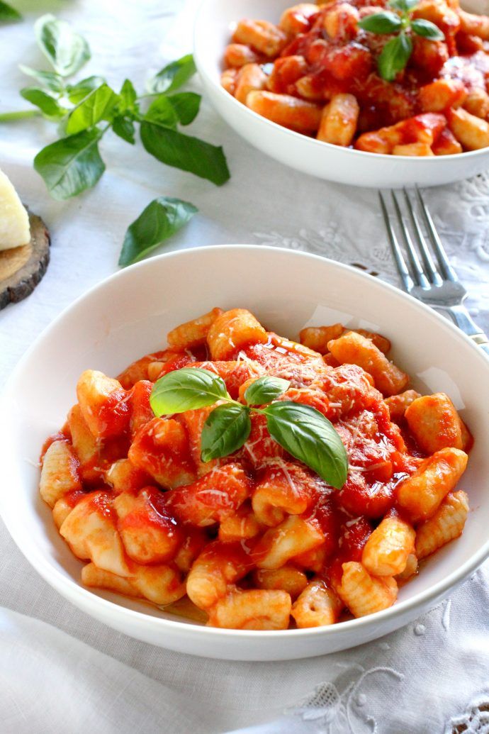 two bowls filled with pasta and sauce on top of a white table cloth next to silverware