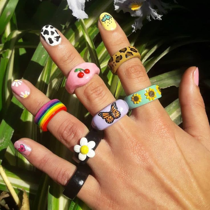 a woman's hand with four different rings on it and flowers in the background