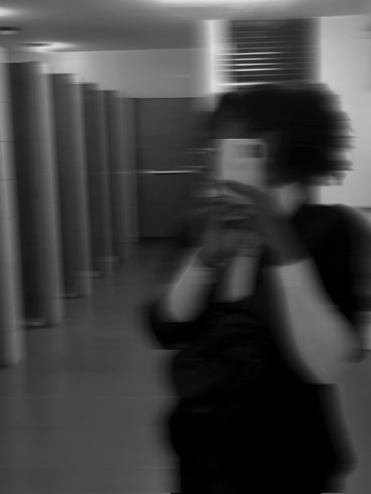 a blurry photo of a person holding a cell phone in an empty room with columns