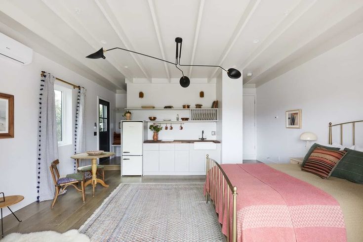 a bedroom with a bed, table and chairs in it next to a kitchen area