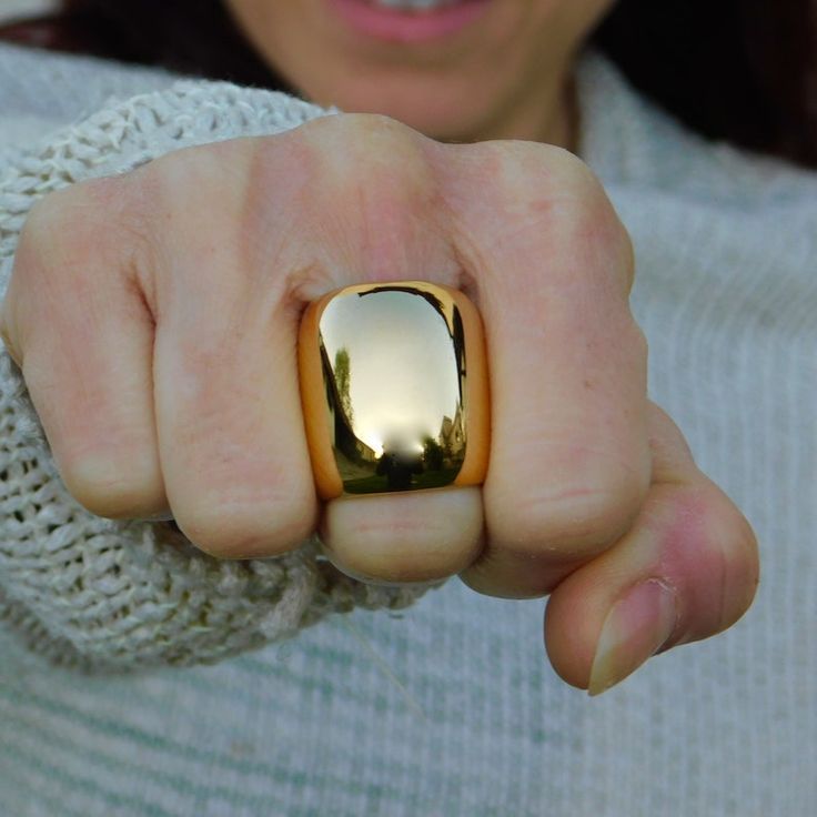 a woman wearing a gold ring with trees reflected in it's reflection on her finger