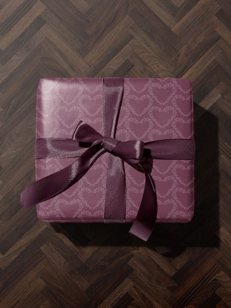 a purple wrapped gift box with a bow on it's side sitting on a wooden floor