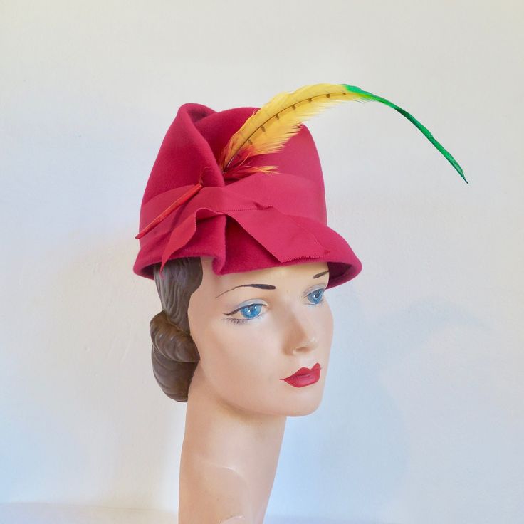 "I believe this hat is from the late 1950's to the early 60's. Made in a vibrant rich magenta pink wool felt. High crown and small brim. Architectural folds on the side brim and crown. Trimmed on the side front with a bright multicolor parrot feather. Magenta grosgrain ribbon trim around the lower crown. Interior crown is also trimmed with magenta grosgrain. Label:  Valerie Modes Condition:  Excellent.  Looks barely worn if at all. Size/Measurements: crown height-  4.75\" brim diameter-  8.75\" Red Retro Party Hat, Retro Red Party Hat, Red Vintage Mini Hats With Curved Brim, Vintage Red Fedora Felt Hat, Red Retro Hat With Curved Brim, Retro Red Hat With Curved Brim, Vintage Red Felt Hat With Curved Brim, Vintage Red Felt Hat With Short Brim, Vintage Red Brimmed Felt Hat