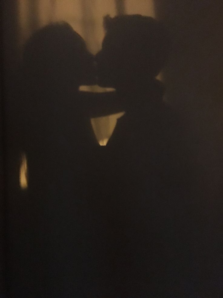 the shadow of two people kissing in front of a window with curtains behind them at night