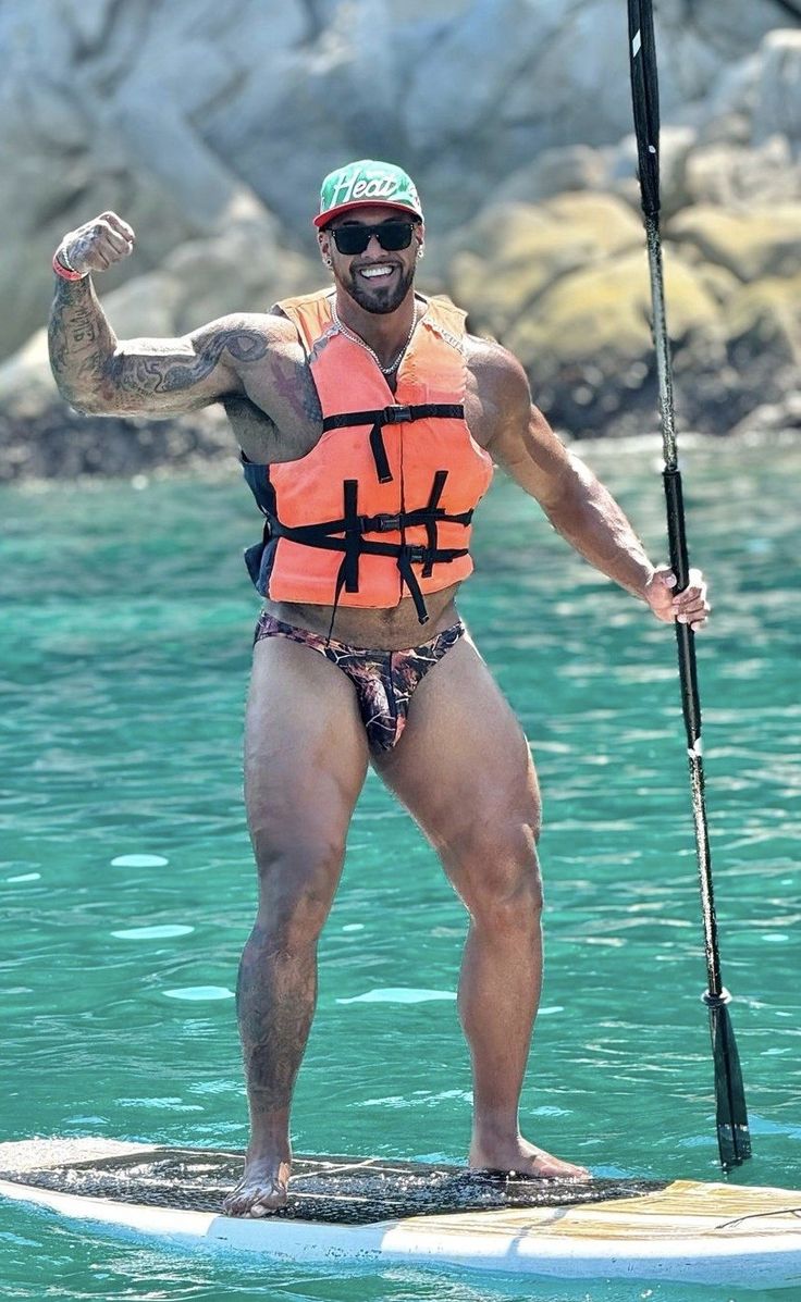 a man standing on a surfboard in the water holding a pole and wearing an orange life jacket