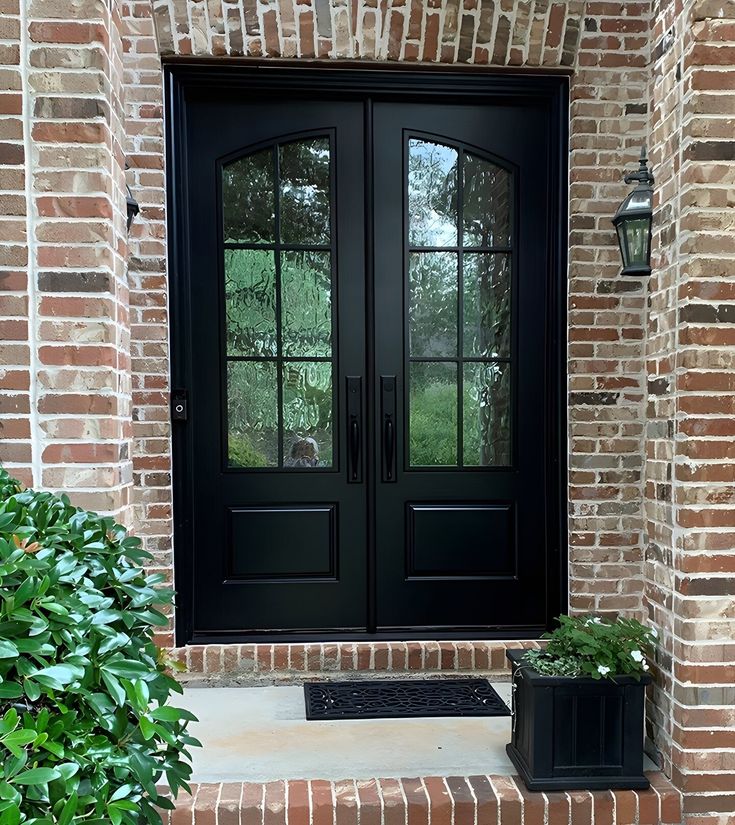 a black double door with two planters on the steps