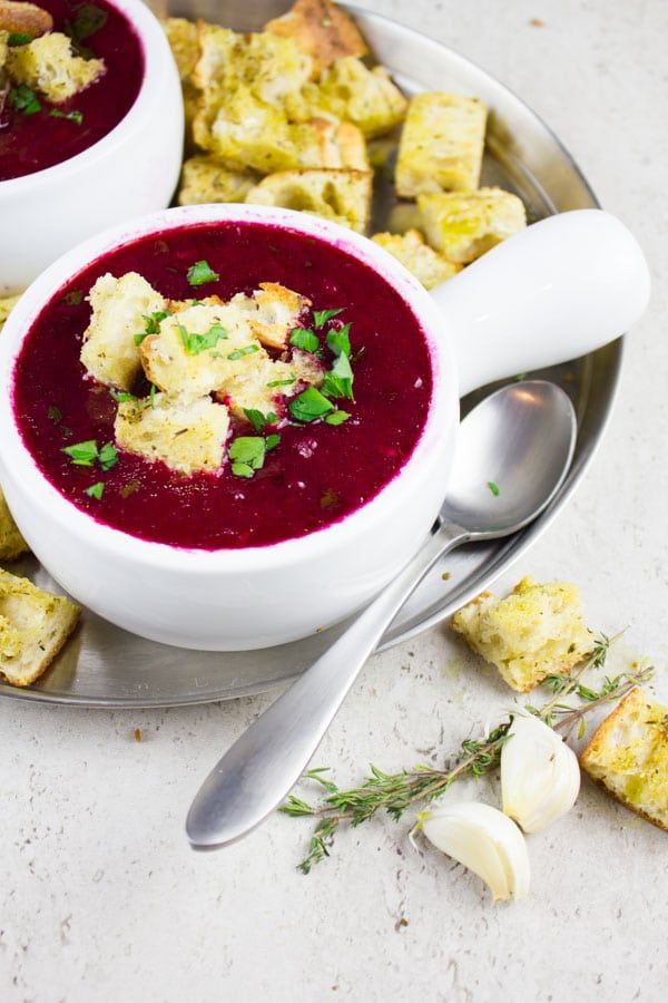 two bowls of soup on a plate with silver spoons and garlic crackers next to it