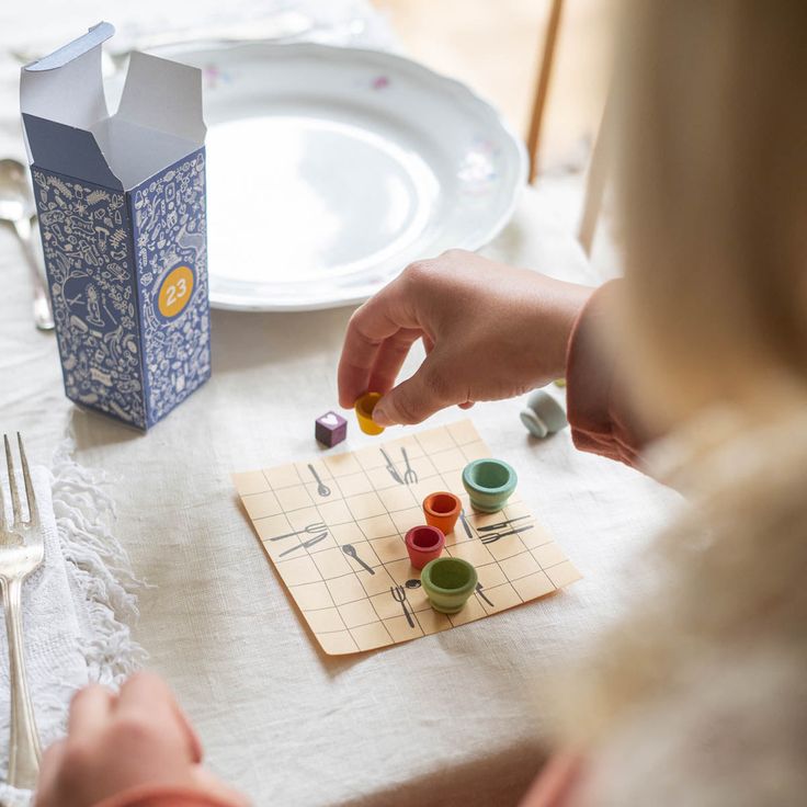 a child is sitting at a table playing with cups and spoons on a board game