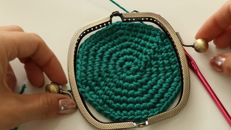 two hands are working on a small green purse with gold trimmings and beading