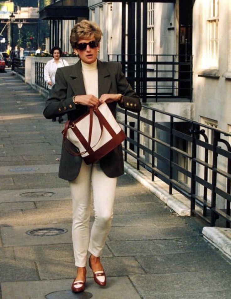 a woman is walking down the street with her purse in hand and she is wearing white pants