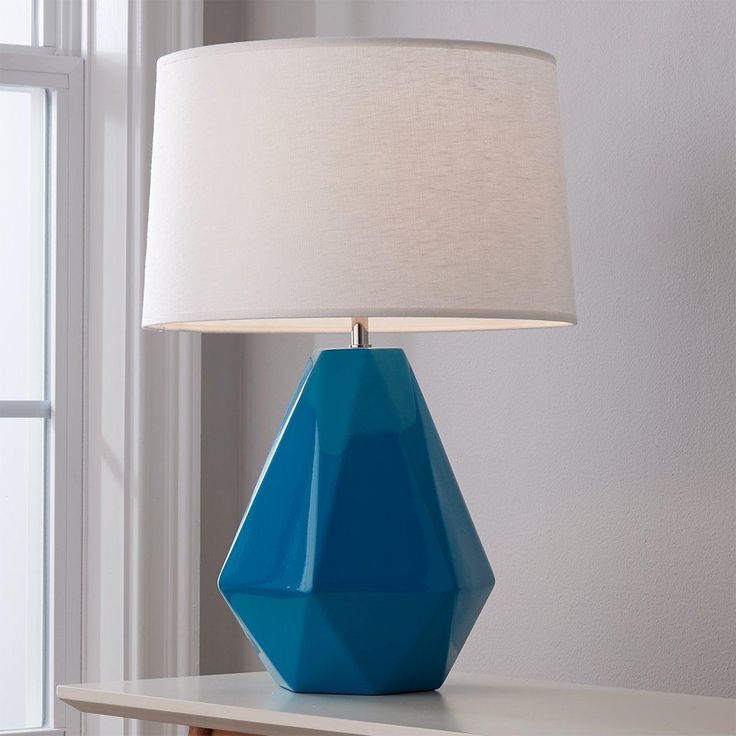 a blue table lamp sitting on top of a white shelf next to a window with a white shade