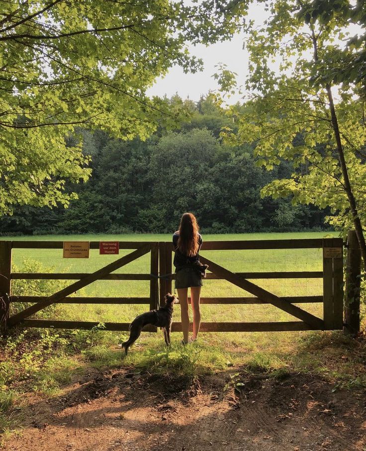 a woman standing in front of a wooden fence with a dog on the other side