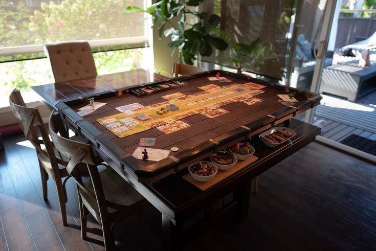 a board game sitting on top of a wooden table next to two chairs and a potted plant