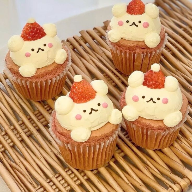 four cupcakes with white frosting and strawberries on top are sitting on a wicker tray