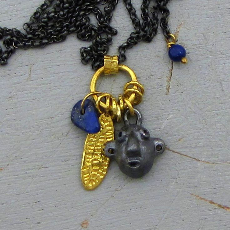 "A beautiful harmony of black oxidized silver chain , 22/24k solid gold, and deep blue Lapiz Lazuli comes together in this 24k gold pendants necklace. A cluster of several pendants hanging on a black silver chain, Lapis Lazuli bead and solid 24 karat gold leaf and a oxidized silver face. The chain is made of oxidized silver chain with 14k gold hoop claps. Dangle Lapis bead is attached to the claps. ~ 24k gold leaf pendant (with the bail): 0.2/0.75\" (5/19 mm). ~ Chain length : 20.5\" (52 cm). Th Blue Oxidized Necklace For Gift, Blue Oxidized Finish Necklace For Gift, Spiritual Blue Hand Forged Necklace, Hand Forged Blue Pendant Necklace, Blue Hand Forged Pendant Necklace, Hand-forged Blue Pendant Necklace, Gold Leaf Pendant, Silver Charm Necklace, Gold Hamsa