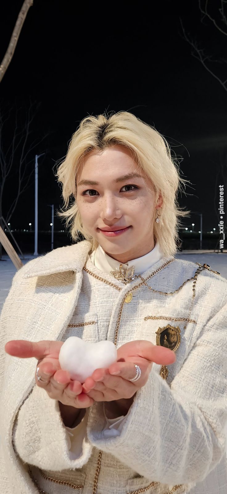 a woman is holding something in her hands while wearing a white coat and gold jewelry