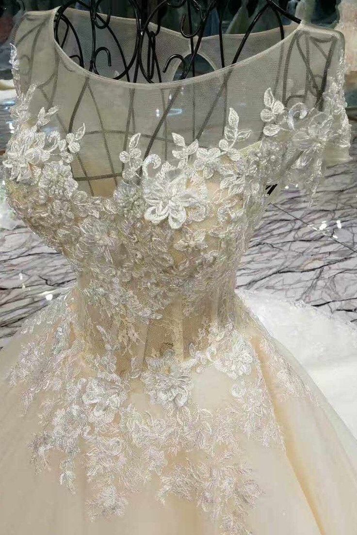 the back of a wedding dress with white flowers on it, in front of an iron rack