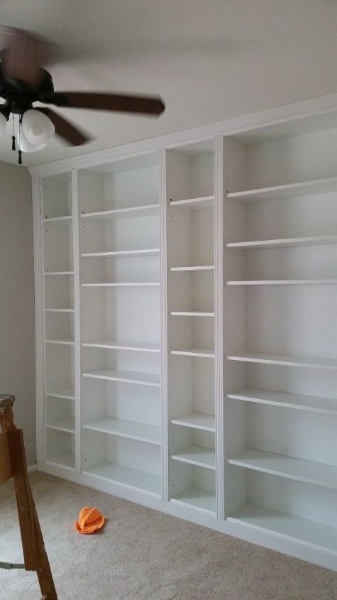 an empty room with white bookcases and a ceiling fan