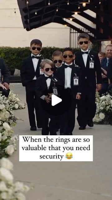 a group of young boys in tuxedos walking down a sidewalk with white flowers