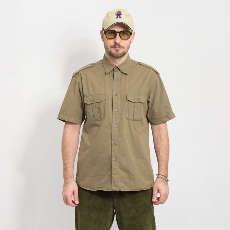 "Vintage short sleeve military shirt in khaki-brown - 2 chest pockets - fastened with metal buttons - materials: 100% cotton Size from the tag: no tag Best fits men: L MEASUREMENTS chest: 48 inches (122 cm) length: 32 inches (81 cm) The model is 6'1\" (186 cm), measures 41-35-39 (104-88-100 cm) and typically wears clothing in size L CONDITION - 8/10 - The shirt in great pre-owned vintage condition. Washed, ready to wear" Khaki Short Sleeve Shirt For Summer Outdoor, Summer Khaki Short Sleeve Shirt For Outdoor, Summer Outdoor Khaki Short Sleeve Shirt, Khaki Collared Camp Shirt For Outdoors, Vintage Khaki Shirt For Summer, Khaki Camp Shirt With Pockets For Outdoor, Short Sleeve Camp Shirt With Button Closure For Outdoor, Short Sleeve Khaki Shirt With Buttons, Outdoor Camp Shirt With Button Closure And Short Sleeves