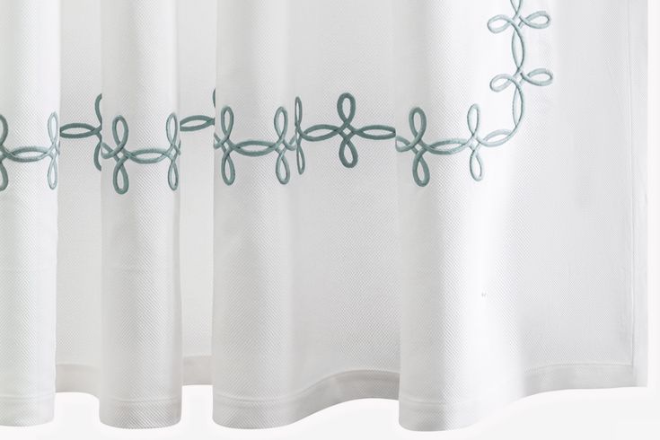 an embroidered curtain hanging on the side of a window with white curtains and green trim