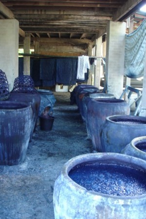 several large blue vases are lined up in a room with clothes hanging on the wall