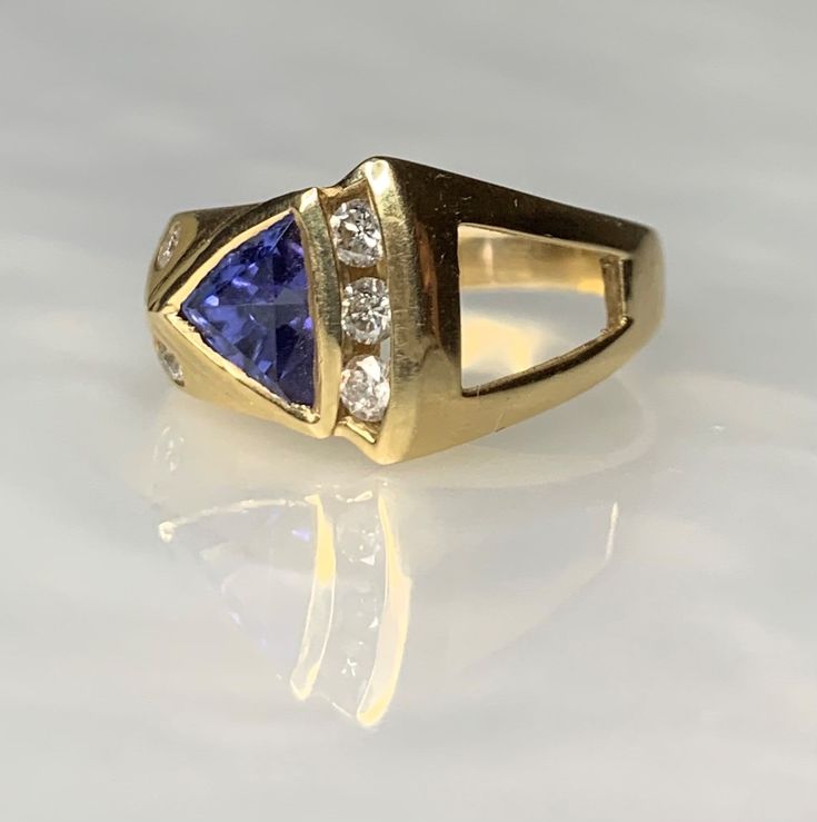 Tanzanite Ring, Trillion Cut Ring, Tanzanite Engagement Ring, Trillion Tanzanite Ring, Geometric Gemstone Ring, Gemstone Engagement Ring A fascinating and shapely vintage tanzanite ring boasting a 1.53 carat trillion cut tanzanite uniquely set on an angle surrounded by sparkling white diamonds weighing 0.48 carats set in solid 14k yellow gold with a modern asymmetric design. *Ring size: US 6 3/4 *Ring weight: 6.54 grams *Complimentary resizing is available up to 3 sizes larger or smaller than st Formal Tanzanite Trillion Cut Ring, Trillion Cut Diamond Ring With Gemstone For Formal Occasions, Formal Trillion Cut Diamond Ring With Gemstone, Fine Jewelry Trillion Cut Sapphire Ring With Accent Stones, Fine Jewelry Yellow Gold Trillion Cut Sapphire Ring, Formal Trillion Cut Multi-stone Jewelry, Sapphire Gemstone Ring, Trillion Cut, Trillion Cut Sapphire Gemstone Ring, Formal Rings With Accent Stones In Trillion Cut