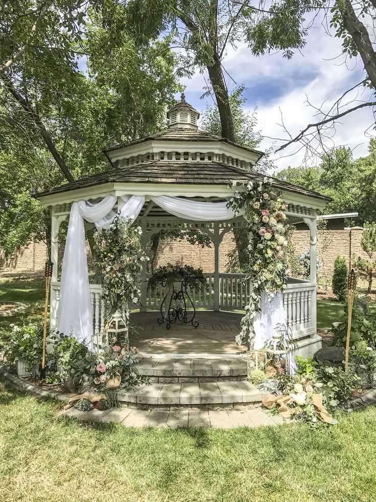 a gazebo with white curtains and flowers on it