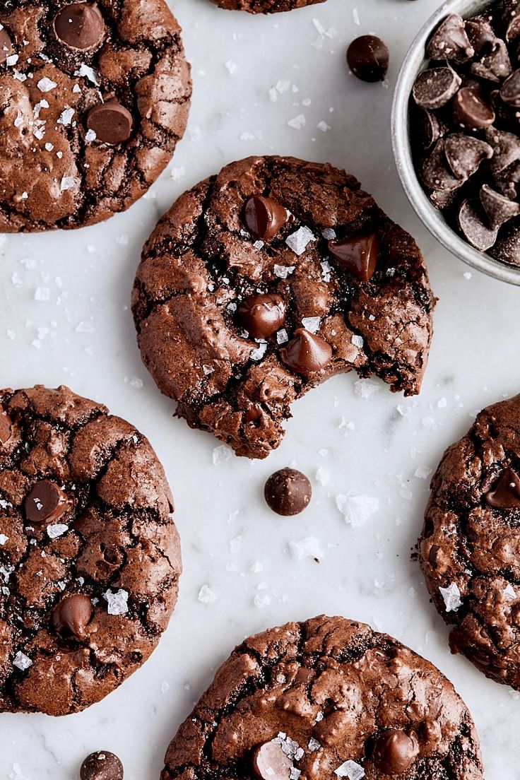 chocolate cookies with sea salt on top and one broken in half, next to a bowl of chocolate chips