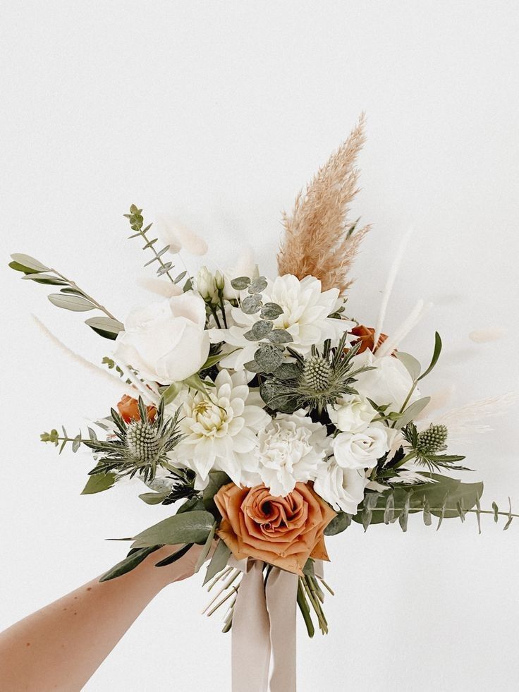 two hands holding a bouquet of white and orange flowers