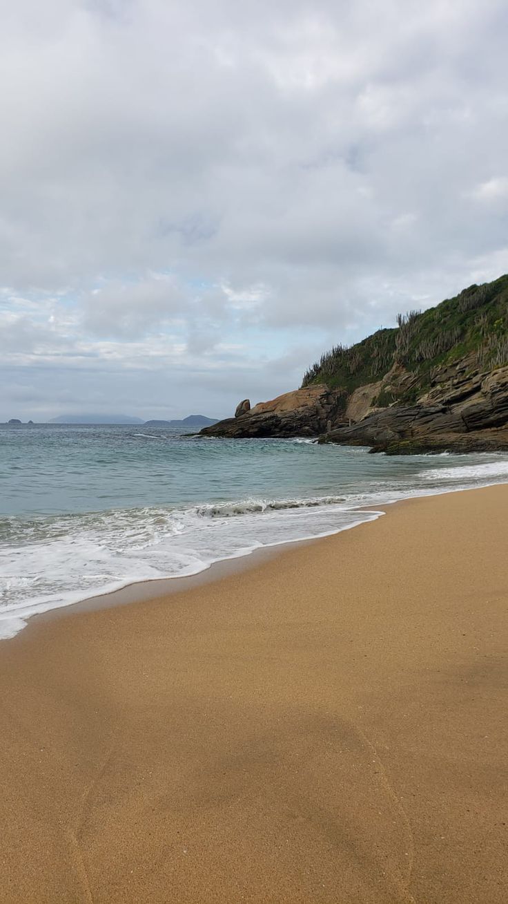 a sandy beach with waves coming in to the shore and an island in the distance