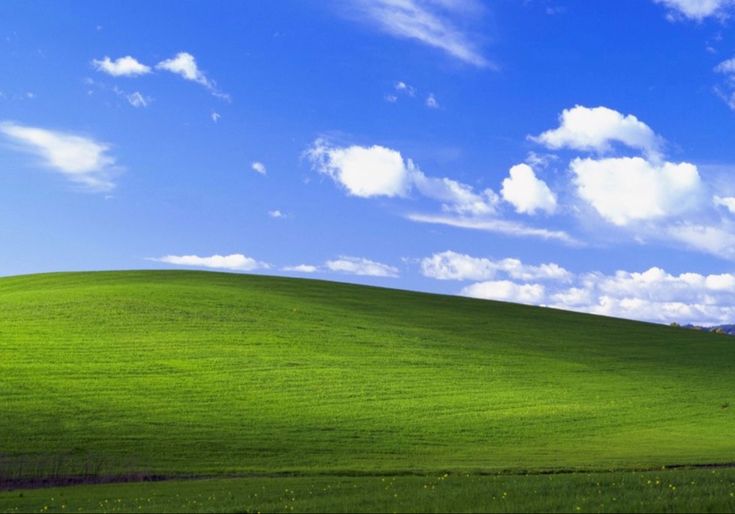 a green field with white clouds in the sky