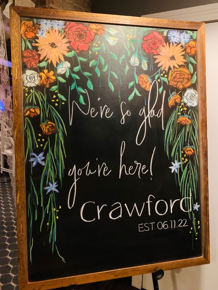 a chalkboard sign with flowers and vines painted on it that says we are so glad you're here, crawford