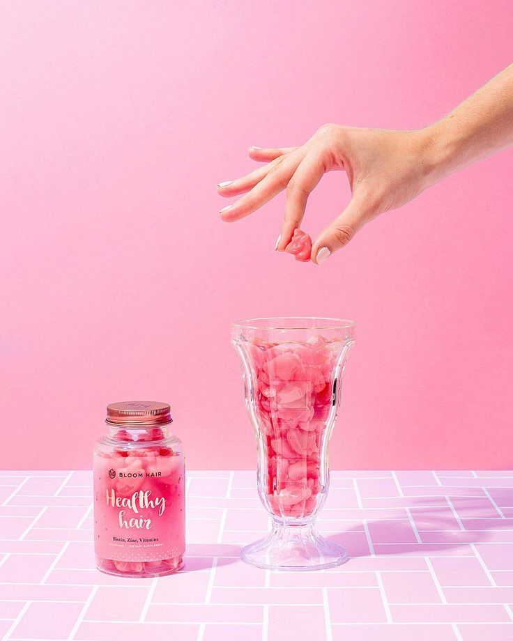 a hand reaching for candy in a glass cup next to a pink background with white tiles