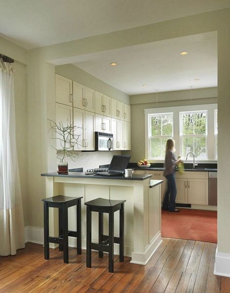 a woman standing in a kitchen next to two stools and a counter with a laptop on it