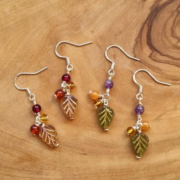 three pairs of earrings with leaves and beads hanging from them on a wooden table top