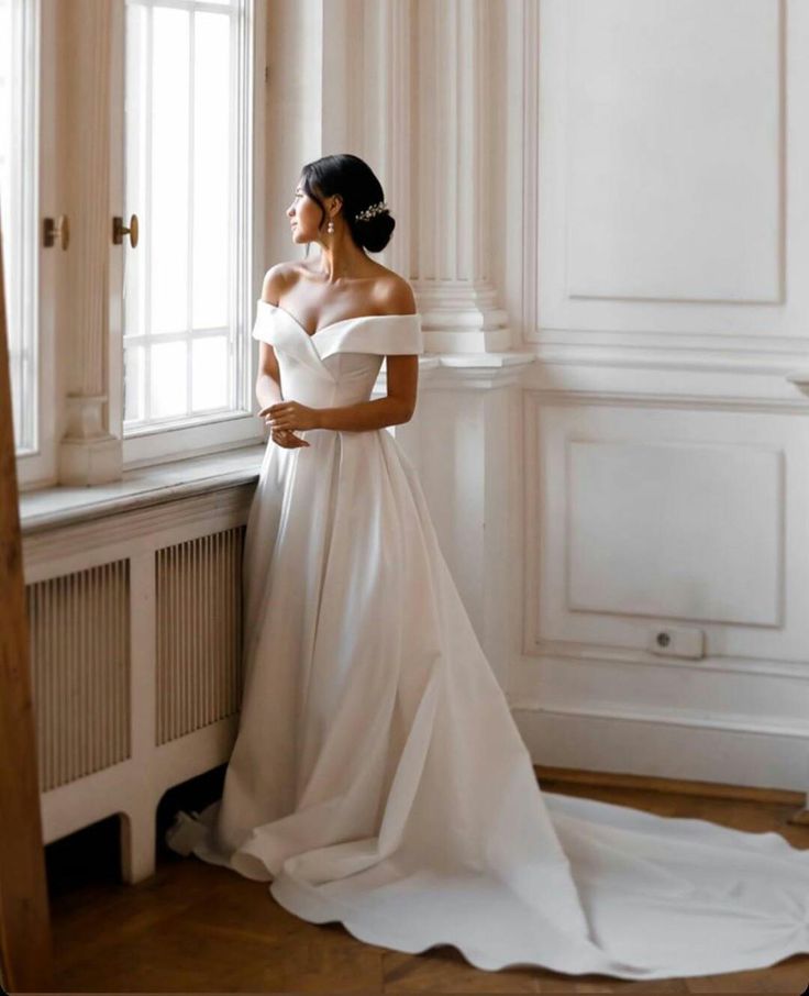 a woman in a wedding dress leaning against a window