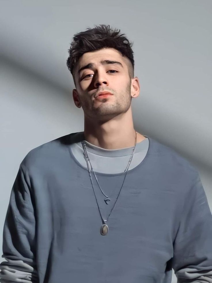 a man with a necklace on his neck looking at the camera while standing in front of a white wall