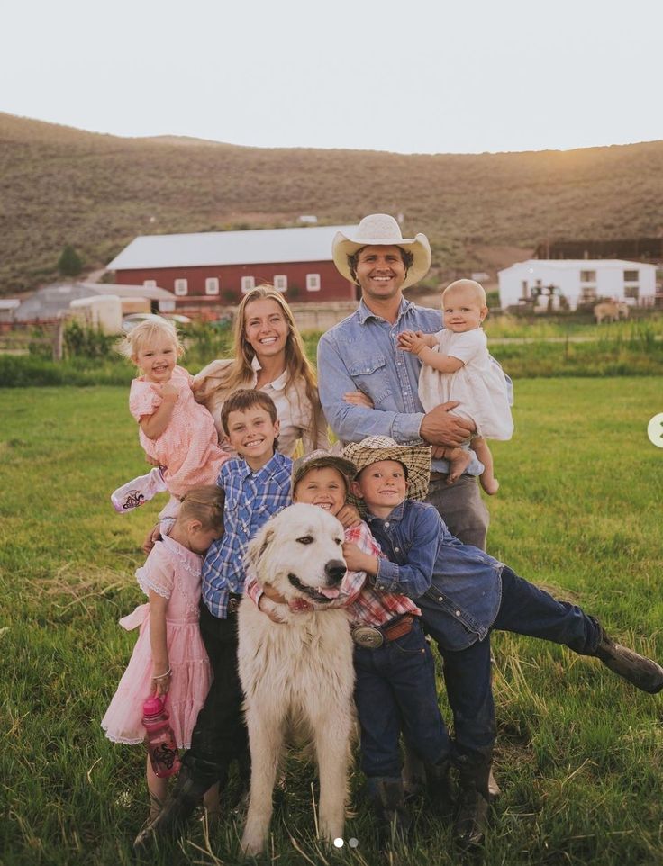 a family poses for a photo with their dog and two children in front of a farm