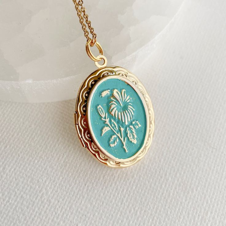 Introducing our stunning oval locket with an embossed hibiscus flower design - a truly unique and charming piece of jewelry. Crafted from high-quality gold plated brass, this locket has a bright, shiny finish and a detailed flat backside that gives it a sophisticated look. Measuring 30mm tall and 23mm wide, this medium-sized locket is perfect for everyday wear. It opens up to reveal a secret place where you can store your most cherished photos, messages, or any other keepsake that holds a specia Oval Cameo Necklace Keepsake, Oval Cameo Necklace For Keepsake, Vintage Personalized Necklace With Flower Pendant, Vintage Personalized Flower Pendant Necklace, Flower Charm Locket Necklace Keepsake, Vintage Charm Locket Necklace With Flower Pendant For Gift, Medallion Locket Necklace With Flower Charm For Gift, Keepsake Flower Charm Locket Necklace, Medallion Locket Necklace With Flower Charm As Gift