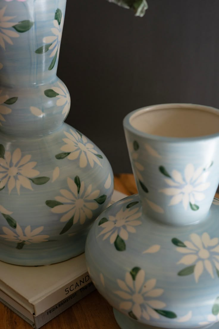 two blue vases sitting next to each other on top of a wooden table near a book