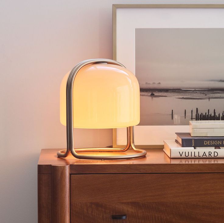 a lamp sitting on top of a wooden dresser next to books and a framed photograph