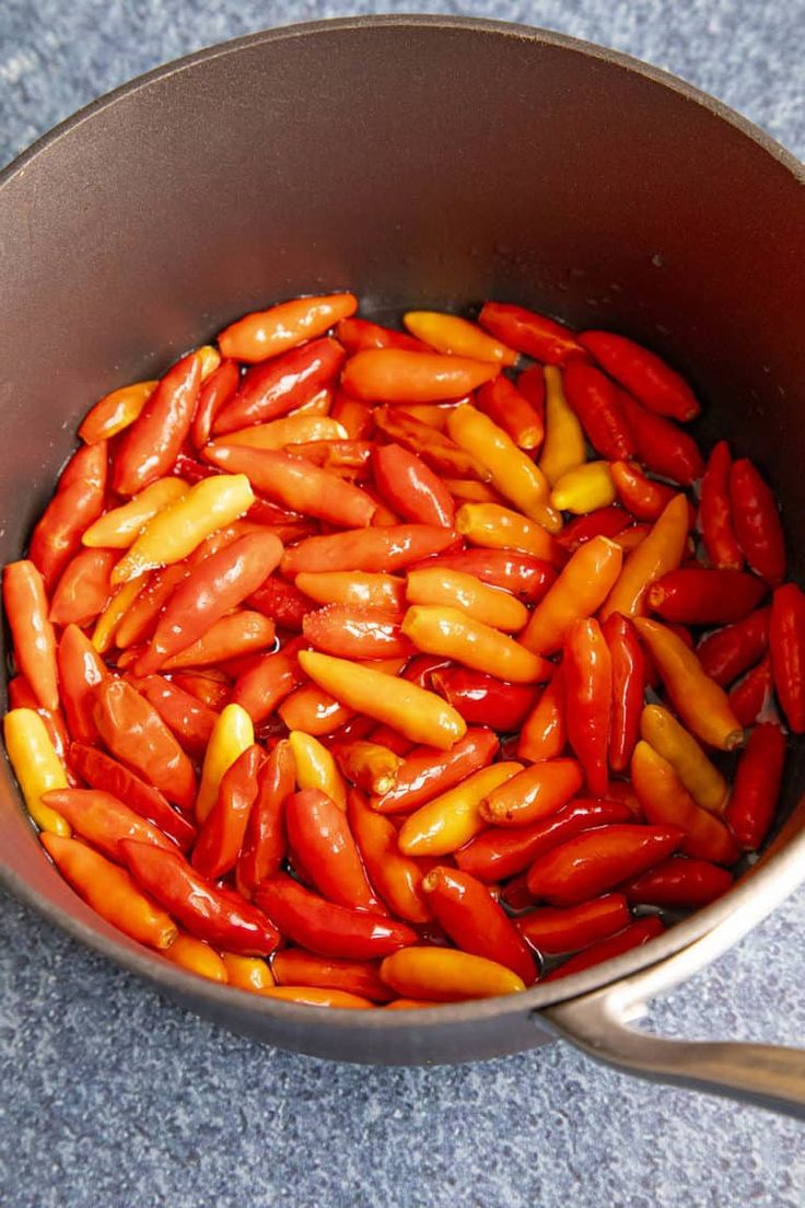 a pan filled with red and yellow peppers on top of a blue countertop next to a wooden spoon