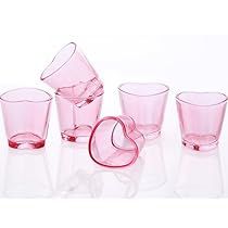 a set of pink glass cups and glasses on a white surface with a red ribbon in the middle