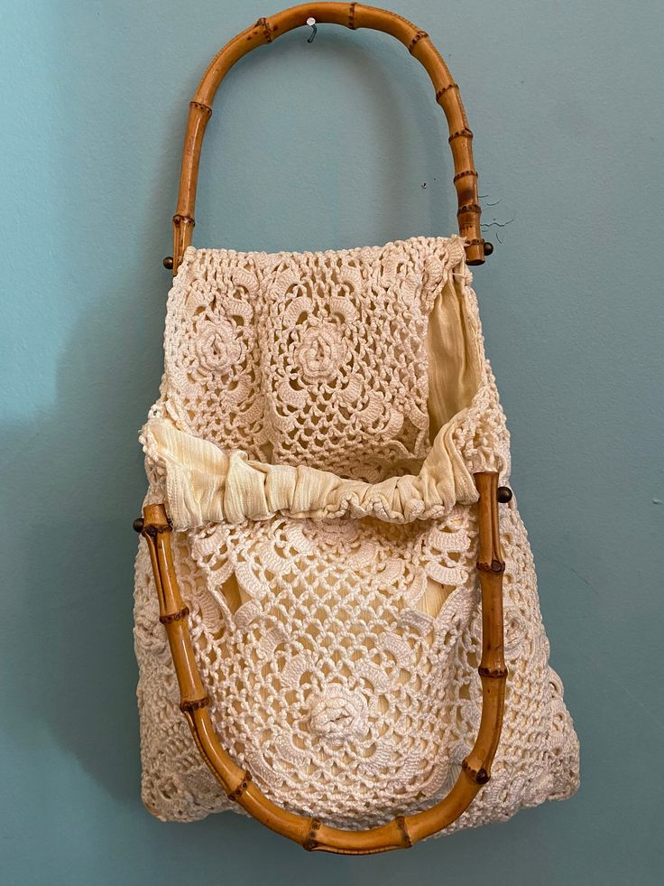 a crocheted bag hanging on the wall with a bamboo handle and strap around it